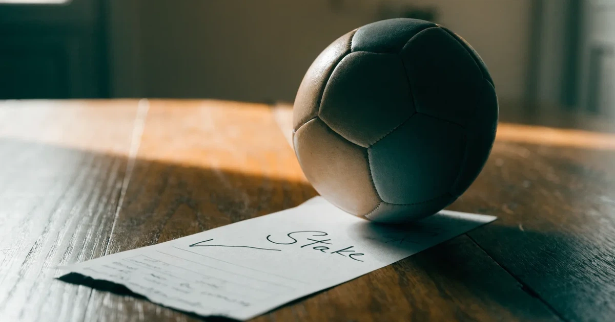 Un pallone da calcio appoggiato su una schedina bianca su un tavolo di legno, alla luce del giorno