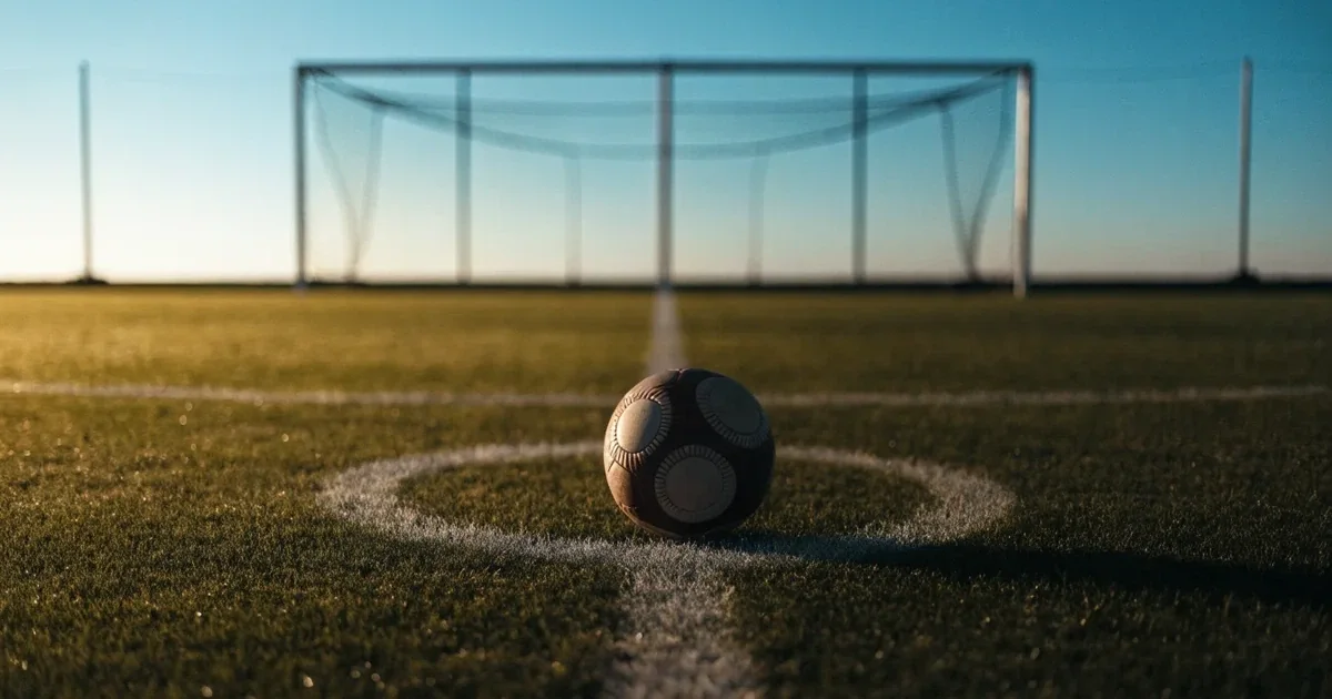 Un pallone da calcio sul dischetto del centrocampo di un prato, alla luce del mattino